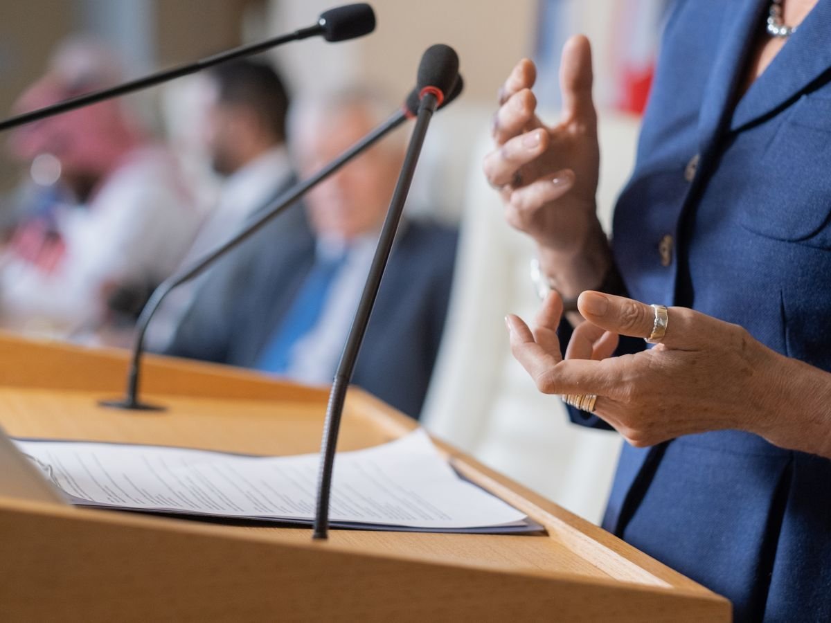 A speaker at a podium addressing a public meeting